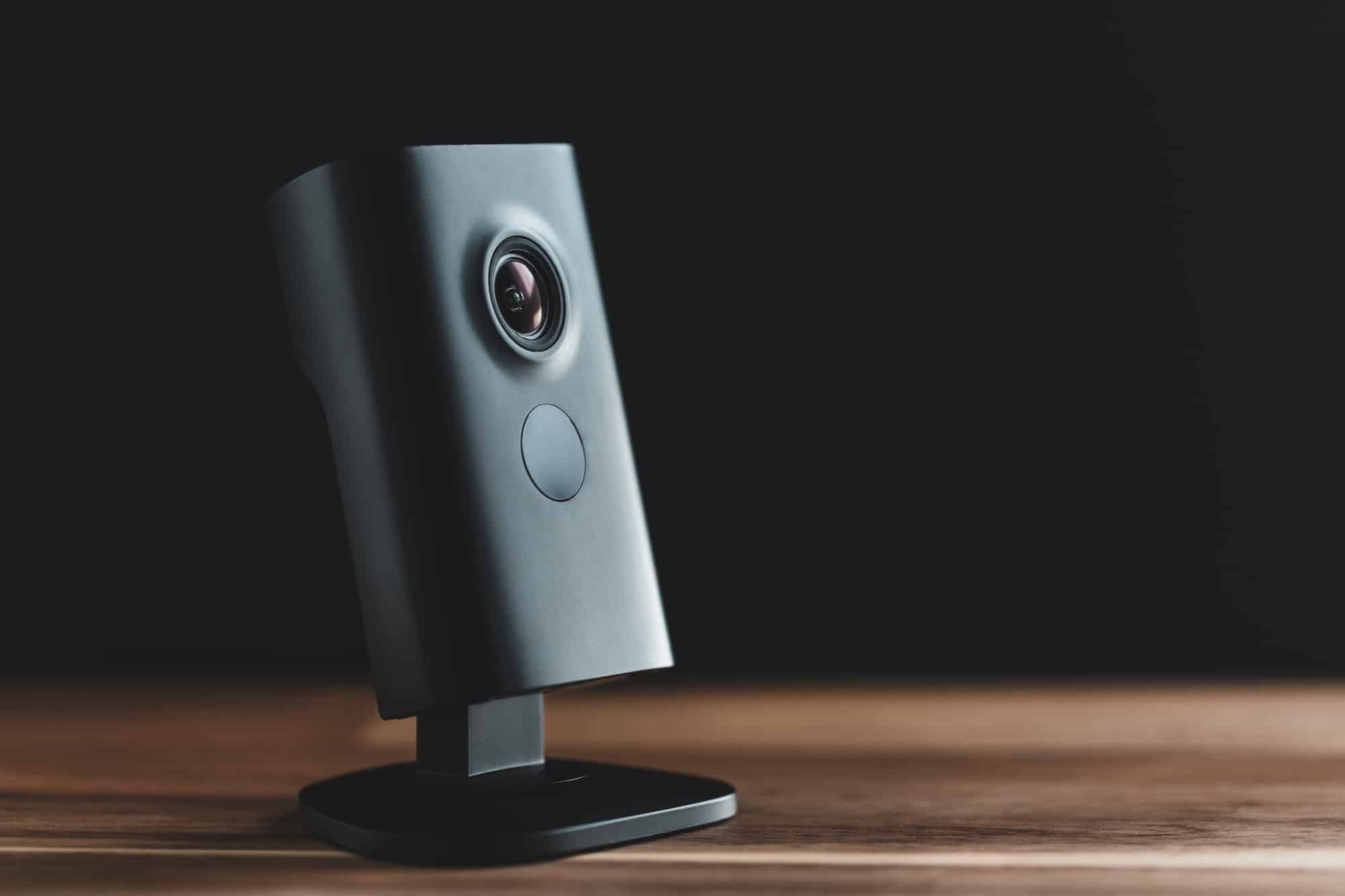 Black minimalist CCTV camera at home on a wooden table.